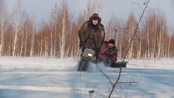 Homem adulto em roupas de inverno rápido equitação e transporte de passageiros no trailer de mini snowmobile através de snowdrifts no campo — Vídeo de Stock