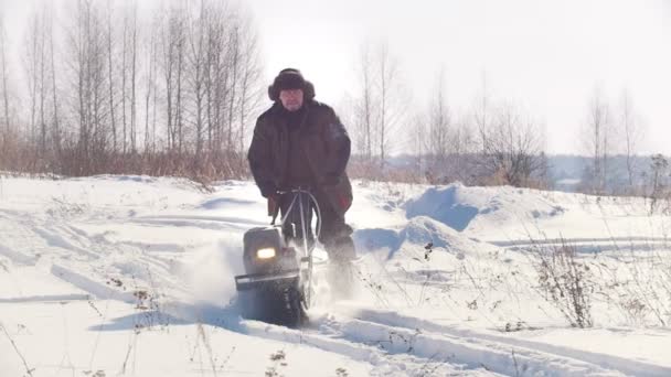 Homem em roupas de inverno montando no rastreador mini snowmobile no inverno através da neve — Vídeo de Stock