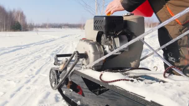 Mann schüttet auf schneeglatter Straße Kraftstoff in den Gastank eines Mini-Motorschlittens — Stockvideo