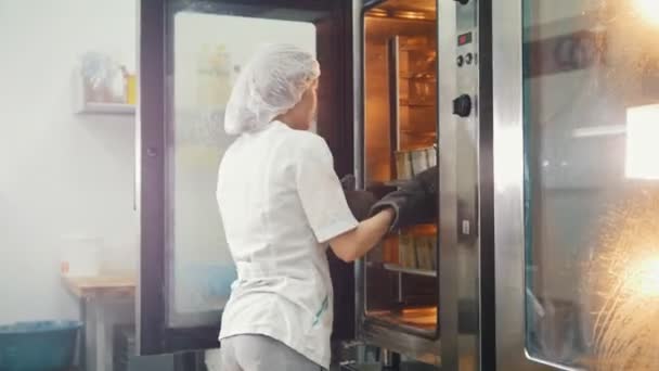 Female bakes on commercial kitchen - pulls the bread from the oven