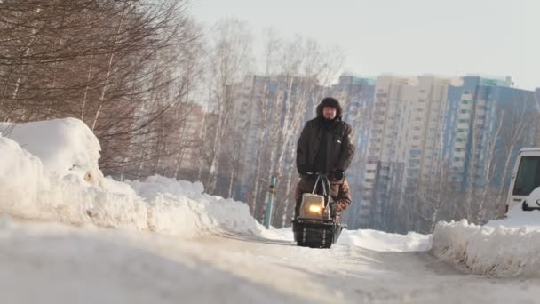 Uomo in abiti invernali in sella a mini motoslitta con rimorchio e passeggero su strada invernale — Video Stock