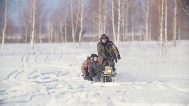 Трое мужчин в зимней одежде едут по зимнему полю на мини-снегоходе с прицепом по глубокому снегу — стоковое видео
