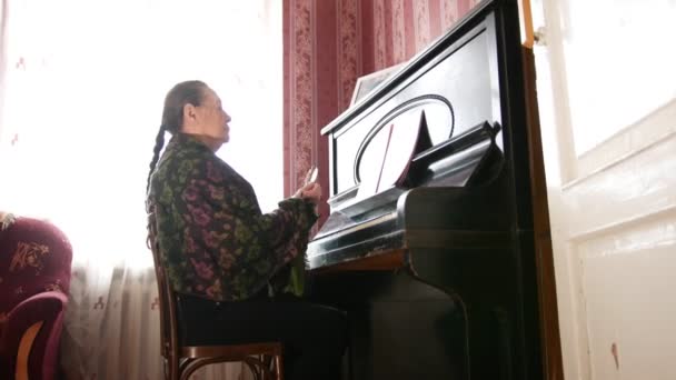 Πορτρέτο της μια ηλικιωμένη γυναίκα με γυαλιά κοντά στο πιάνο — Αρχείο Βίντεο
