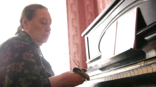 Senior kvinna är rengöring sin glasögon nära piano — Stockvideo