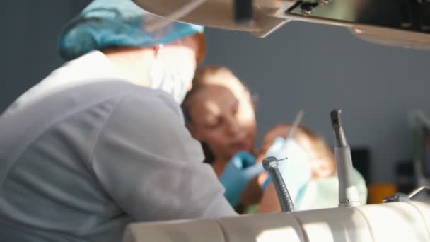 Dentista examinando y consultando a la hija sentada en las rodillas de su madre — Vídeos de Stock