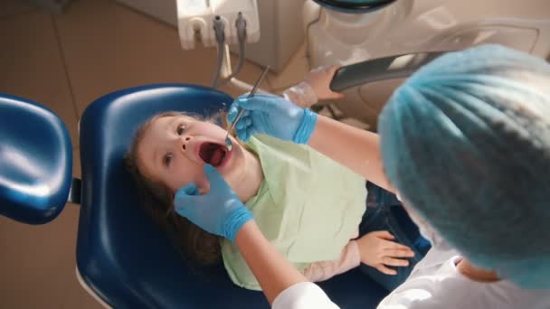 Chica en recepción en el dentista, el estomatólogo examina los dientes de los niños, linda y traviesa chica sonriendo — Vídeo de stock