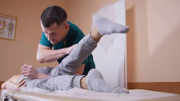 Chiropratico massaggiare una giovane donna sdraiata su un lettino da massaggio, allungando e flettendo l'articolazione dell'anca premendo sul ginocchio — Foto Stock