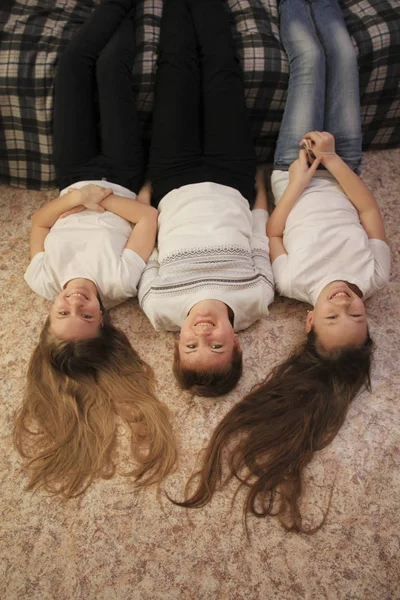 Retrato de mamá joven y sus dos hijas adolescentes tumbadas en el suelo en casa, sus pies en el sofá — Foto de Stock