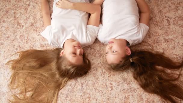 Две девочки-сестры-подростки лежат на полу, их волосы раскиданы по полу — стоковое видео