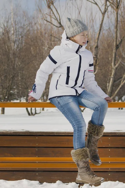 Tiener meisje het dragen van warme kleren wandelen buiten in de winter, zittend op de Bank — Stockfoto