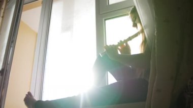 Genç sevimli genç kız evde pencere kenarında oturan flüt çalmaya