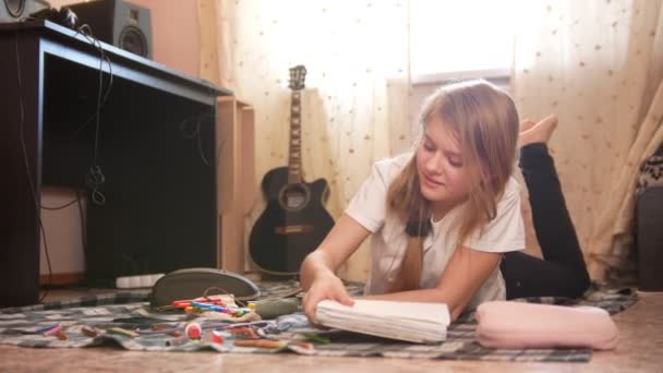 Дівчина-підліток проводить час вдома малюючи, лежачи на підлозі — стокове відео