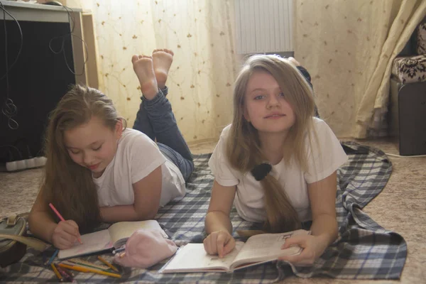 Две девочки-подростка, которые проводят время дома, читая книгу и рисуя, лежа на полу — стоковое фото