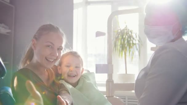 Petit enfant avec maman dans la chaise de stomatologie montrant grand doigt vers le haut — Video