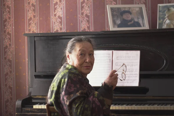 La anciana sentada frente a un piano con sus gafas en las manos — Foto de Stock