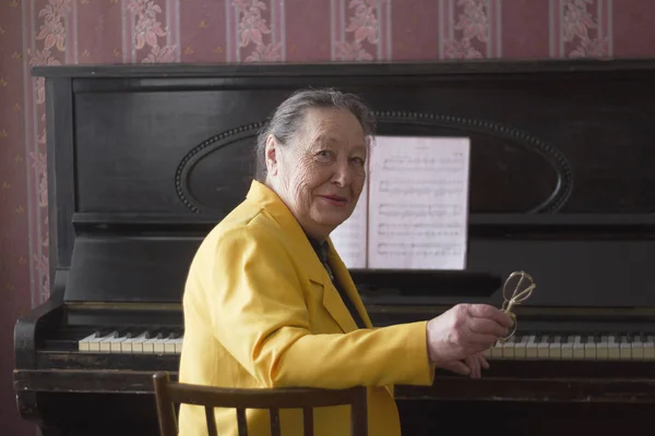 Vieja encantadora pianista con la chaqueta amarilla sentada al piano — Foto de Stock