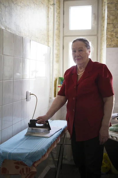 Mulher idosa na blusa vermelha passando uma toalha em casa — Fotografia de Stock