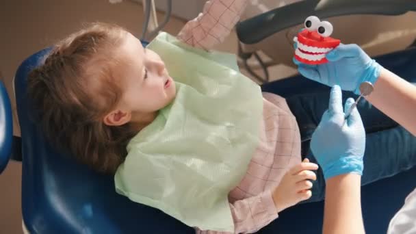 Bambina seduta sulla sedia dentale a giocare con strumenti e giocattoli dentali — Video Stock