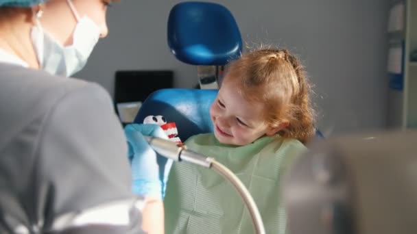 Niña sentada en silla dental jugando con herramientas y juguetes dentales, preparación para la limpieza de dientes — Vídeo de stock