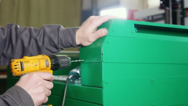 Рабочий человек с помощью электрической ручной дрели - делает отверстие в зеленой металлической машине — стоковое видео