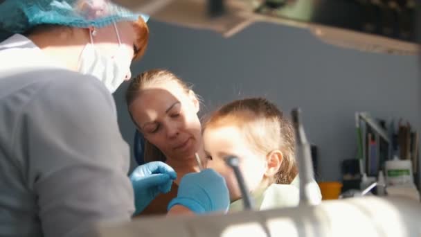 Девушка на ресепшене у дантиста, стоматолог осматривает зубы ребенка, непослушная девочка улыбается — стоковое видео