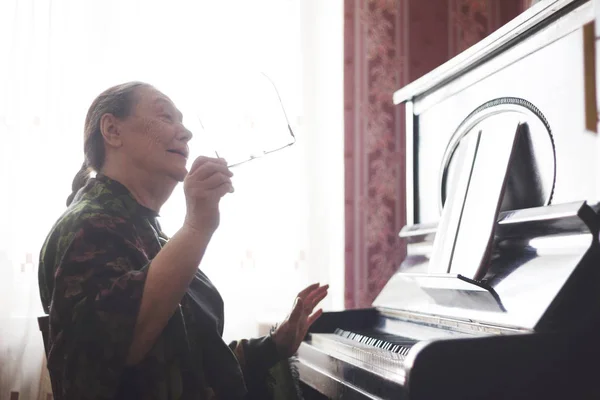 Wanita tua duduk di depan piano dan menyanyikan sebuah lagu — Stok Foto