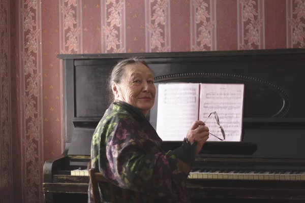 Retrato de una anciana sentada frente a un piano con sus gafas en las manos — Foto de Stock
