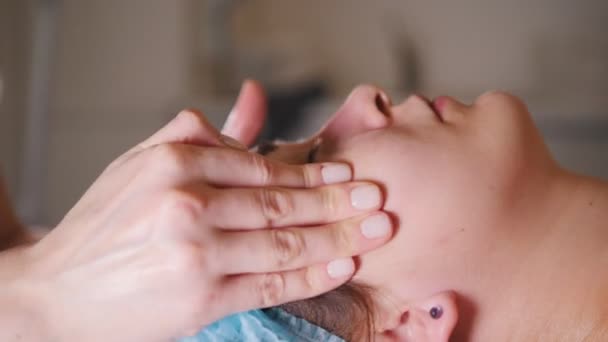 Visage d'une jeune femme dont l'esthéticienne fait un massage facial dans un salon de beauté — Video