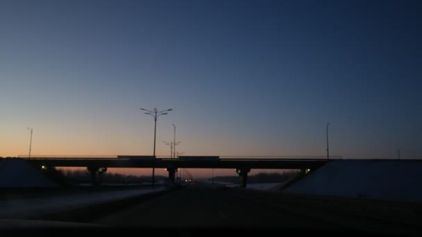 Vista da janela do carro movendo-se em uma estrada de inverno crepúsculo escuro, trilha sob a ponte — Vídeo de Stock