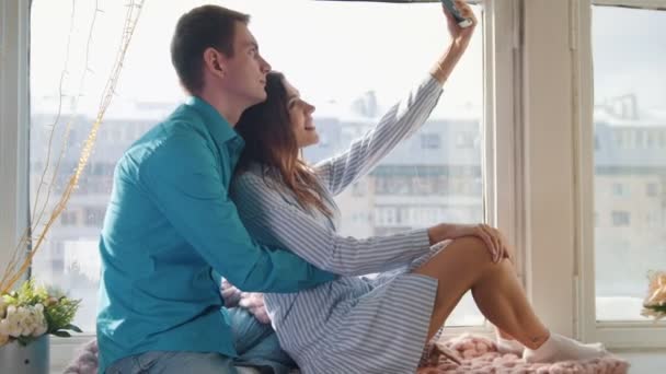 Feliz alegre amante pareja haciendo selfie en ventana, joven atractivo chico y chica — Vídeos de Stock