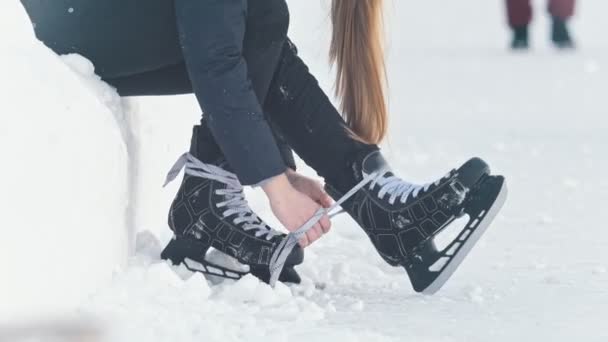 Підліток довгошерста дівчина сидить на снігу, затягуючи шнурки на ковзанах і посміхаючись — стокове відео