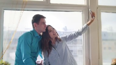 Genç ve çekici erkek ve kadın pencerenin önünde oturan bir selfie yapıyor