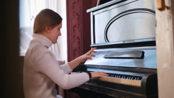 Chica adolescente sonríe y toca en el piano — Vídeo de stock