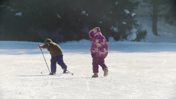 喀山, 俄罗斯-2018年3月: 两个孩子在冬季散步, 一个男孩滑雪和下降, 一个女孩步行, 一个成年滑雪者骑过他们 — 图库视频影像