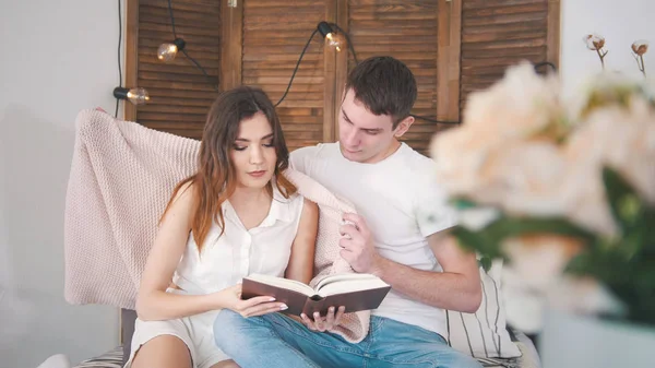 Молодой человек и женщина отдыхают дома - читая книгу на диване целуя друг друга счастливыми — стоковое фото