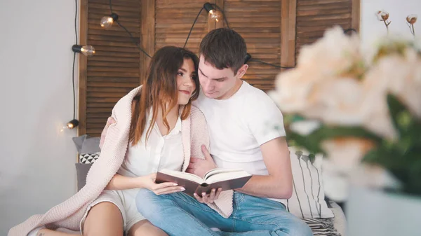 Young man and woman relaxing at home - reading the book on sofa kissing each other happy