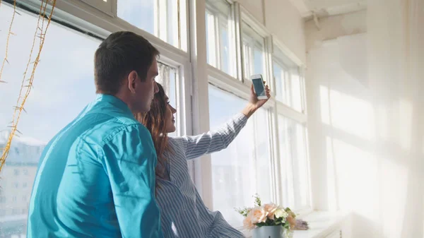Feliz alegre amante pareja haciendo selfie en ventana, joven atractivo chico y chica —  Fotos de Stock