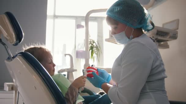 Chica en recepción en el dentista, el estomatólogo examina los dientes de los niños, linda y traviesa chica sonriendo — Vídeo de stock