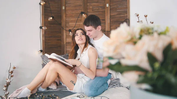 Młody mężczyzna i kobieta relaks w domu - czytanie książki na kanapie całując szczęśliwy — Zdjęcie stockowe