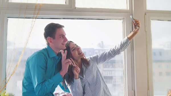 Mladá a atraktivní muž a žena, která dělá selfie sedět u okna — Stock fotografie