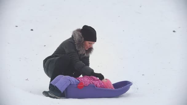 Mamá hablando con su hijita, que yace en un trineo en el parque de invierno — Vídeos de Stock