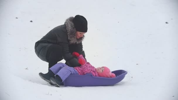 Мама сидит его непослушная дочь в санях на зимней улице — стоковое видео