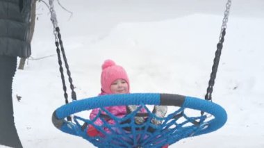 Kışın üzerinde parkta salıncakta sallanan sevimli küçük kız