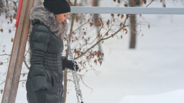 Moeder haar schattig dochtertje swingen op een schommel in de speeltuin in de winter — Stockvideo