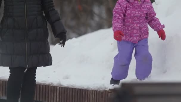 Niña linda caminando en la nieve y cayendo en el banco de nieve para un paseo con su mamá — Vídeo de stock