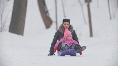 Genç anne ve sevimli kızı kızak kış Park sürme