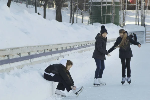 Adolescente assise sur la neige serrant les lacets sur les patins — Photo