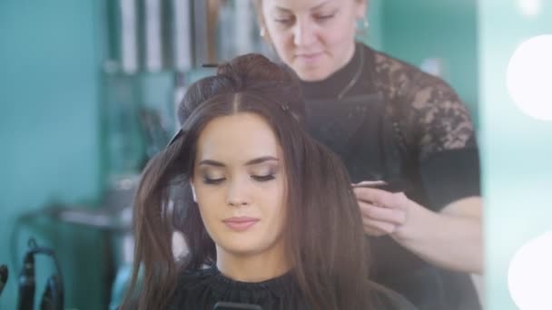Mladá brunetka v salonu krásy, vizážistka dělá make-up, kadeřnictví je úprava vlasů — Stock video