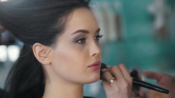 Estilista profesional hembra haciendo maquillaje para mujer joven delante del espejo en el salón de belleza — Vídeos de Stock