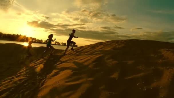 Un grupo de atletas - dos chicas y un chico huyen de la montaña, cerca del río al atardecer — Vídeos de Stock